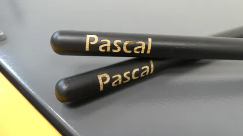 Detailed macro view of name Pascal laser engraved with micro-precision on stacked black wooden drumsticks.