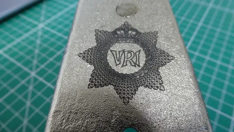 Micro close-up of a laser engraved military crest showing crisp cross-hatch vector details on steel.